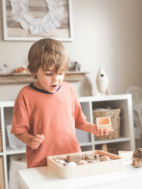 boy in orange crew neck t-shirt standing in front of white wooden table with cupcakes